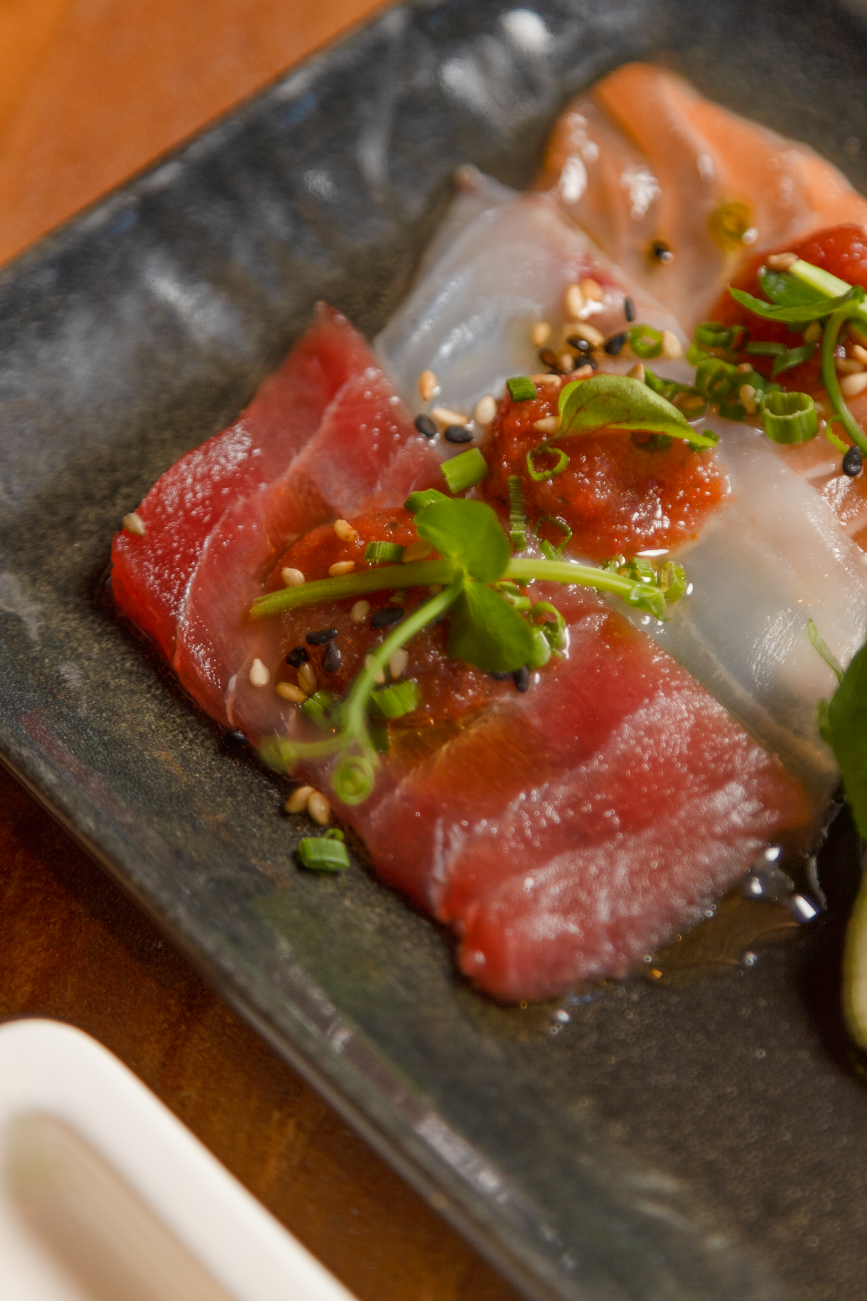 Fette di sashimi con erbe e condimenti su piatto nero