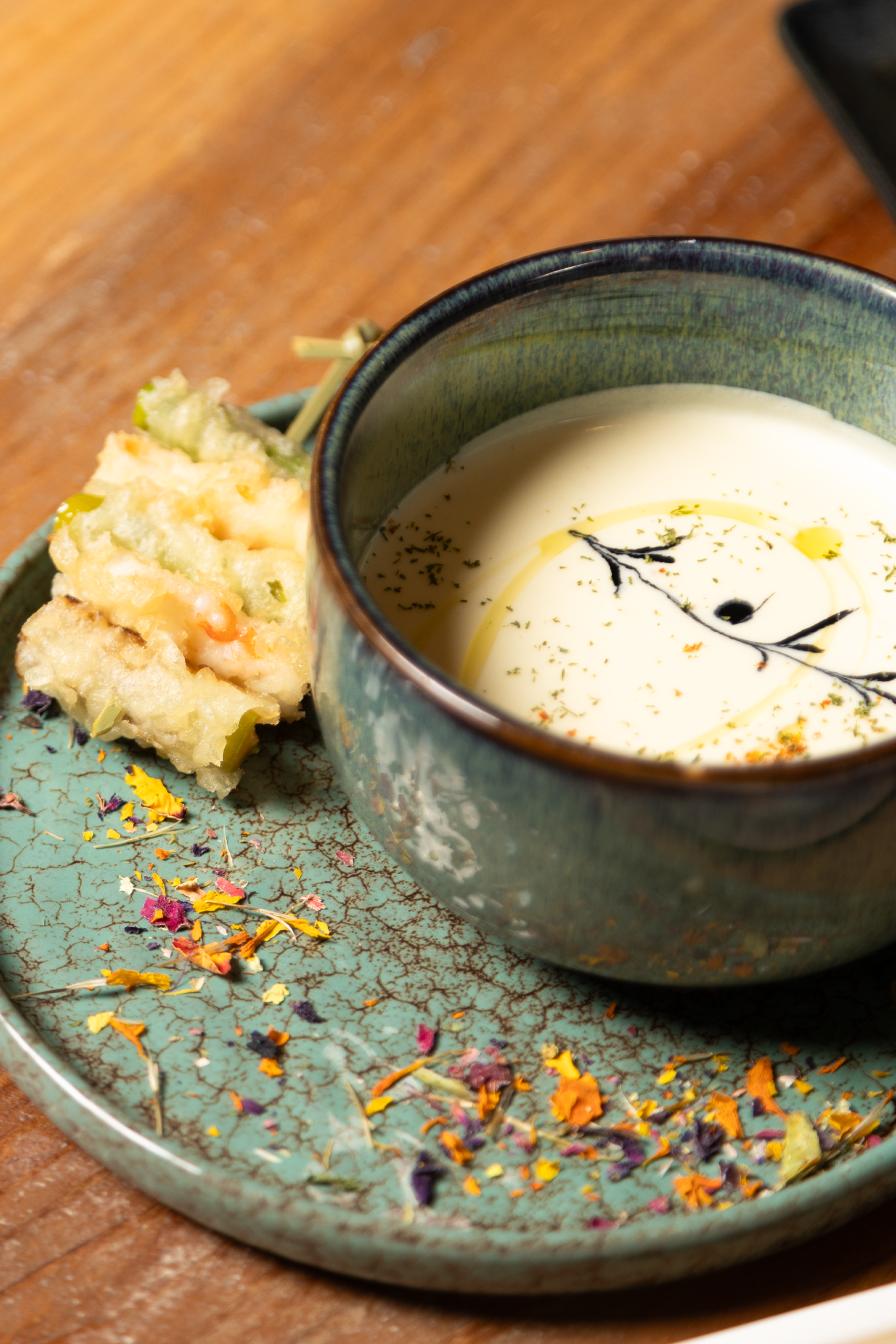 Zuppa cremosa in ciotola su piatto decorato con fiori secchi.
