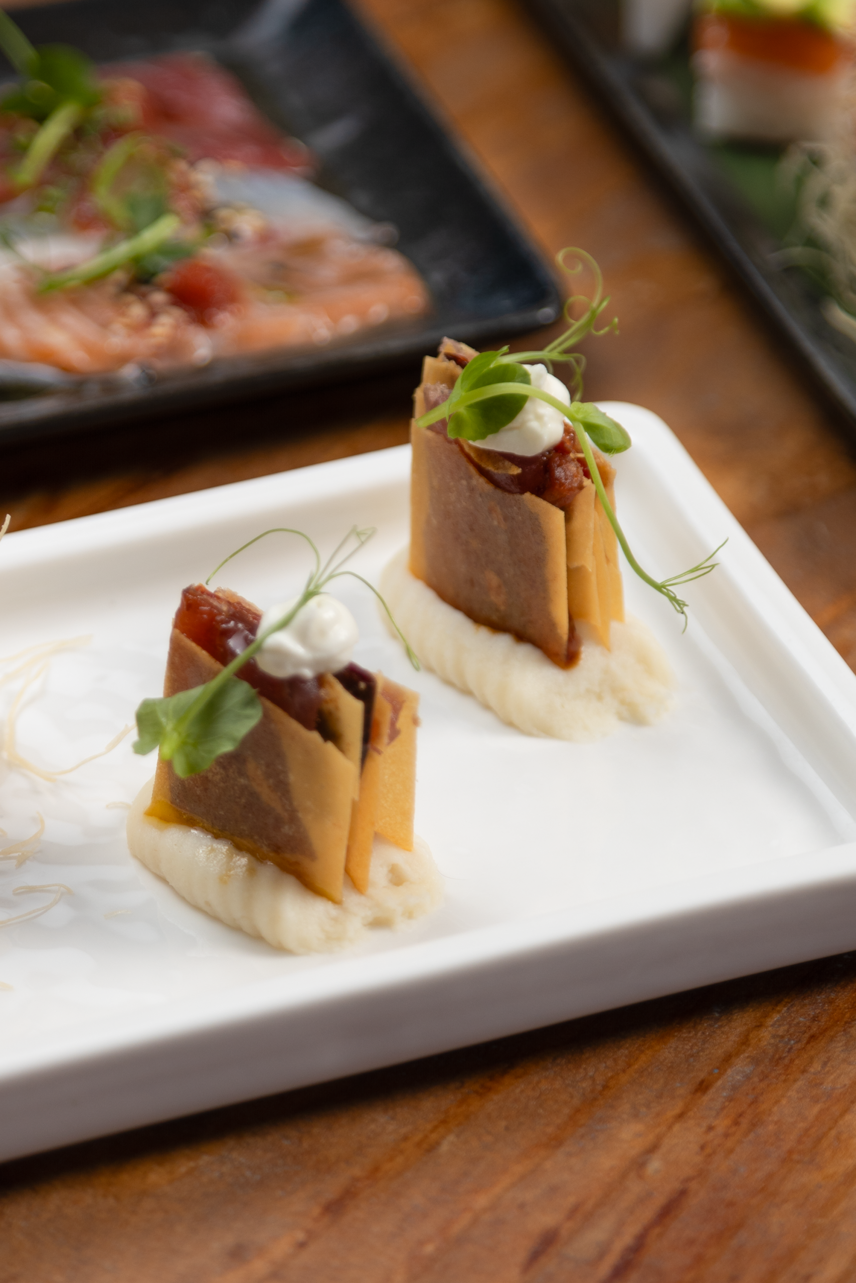 Due porzioni di antipasto gourmet su un piatto bianco decorato con panna e germogli.