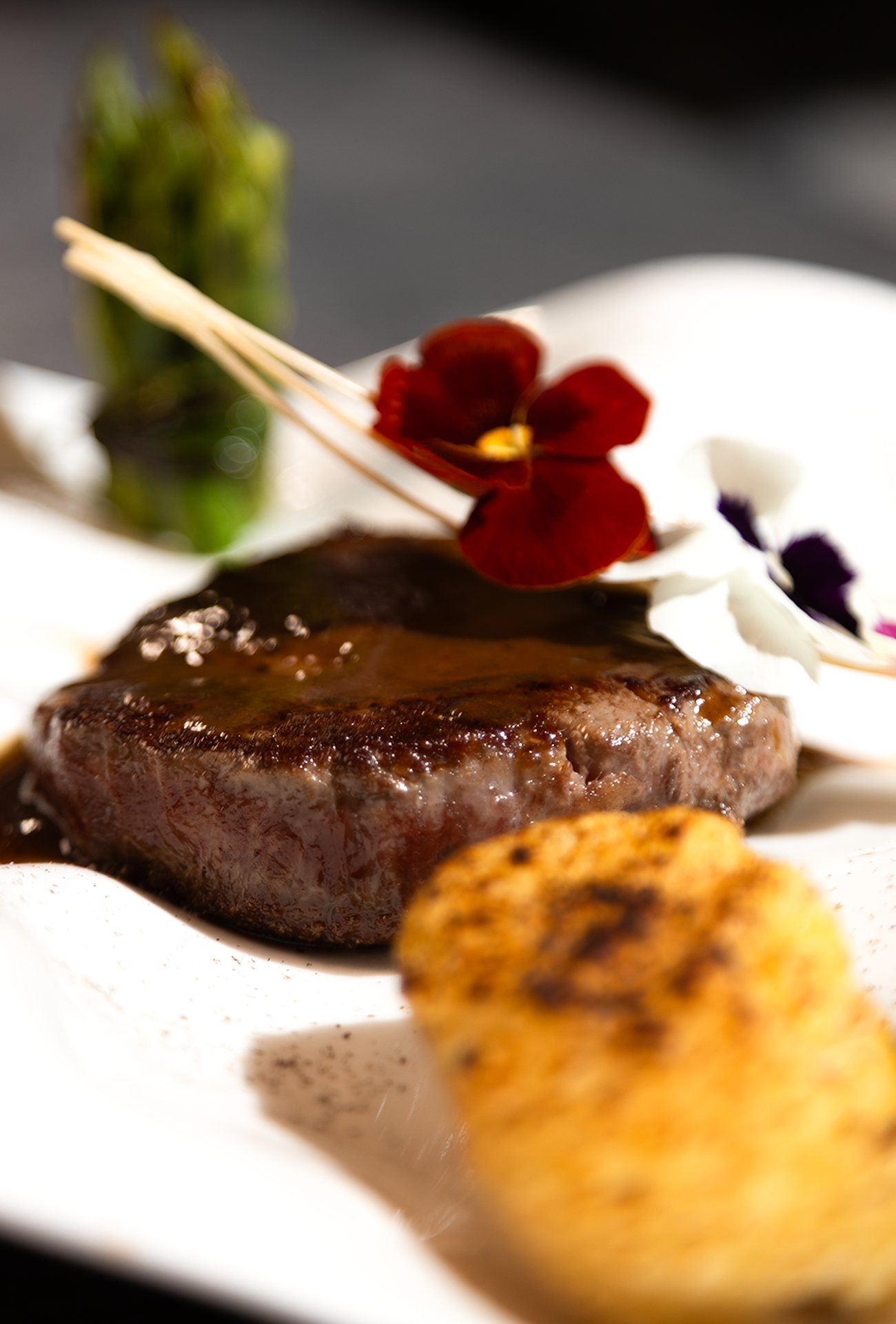 Filetto di carne con fiori commestibili e contorno su piatto bianco.